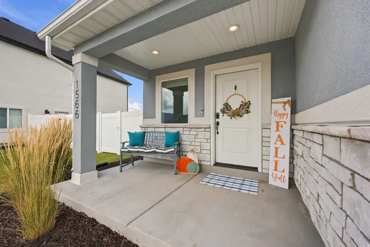 Covered concrete porch with recessed lighting, stone veneer accents, and a white entry door