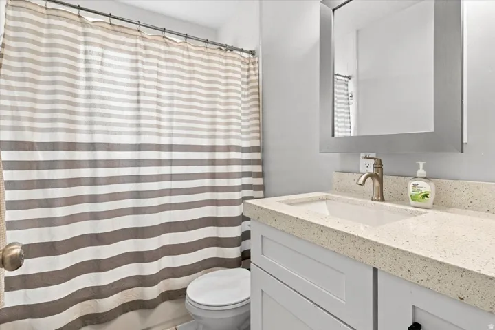 Vanity with an integrated rectangular sink, speckled countertop, brushed nickel faucet, and a wall-mounted mirror
