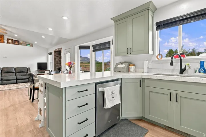Kitchen featuring light green cabinetry, white countertops, stainless steel dishwasher, and a black faucet