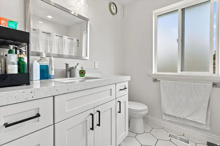 White shaker-style cabinetry with matte black hardware, speckled countertop, undermount sink with chrome faucet, hexagonal floor tiles, and a privacy window