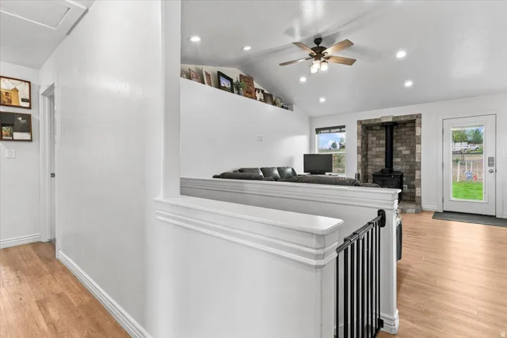 Vaulted ceiling with recessed lighting and a ceiling fan, wood-finish flooring, stone-finish fireplace surround, and a full-light rear door