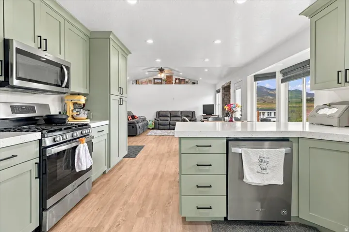 Kitchen featuring light green cabinetry, stainless steel appliances, light-toned countertops, wood-finish flooring, and recessed lighting