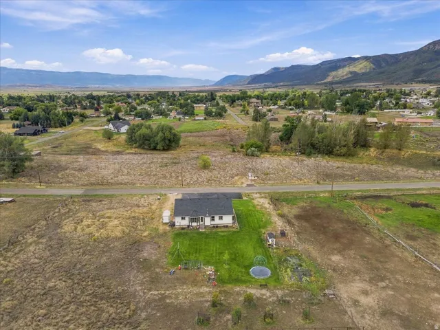 Expansive lot featuring a single-story residence with a dark roof and light-colored siding, a large grassy yard, and surrounding natural landscape