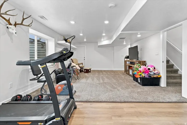Recessed lighting illuminates this space featuring a combination of carpet and wood-finish flooring, a functional window, and white painted walls
