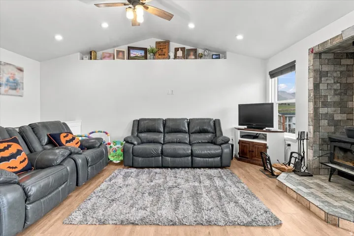 Vaulted ceiling with recessed lighting and ceiling fan, wood-finish flooring, stone-clad fireplace, and an elevated display shelf