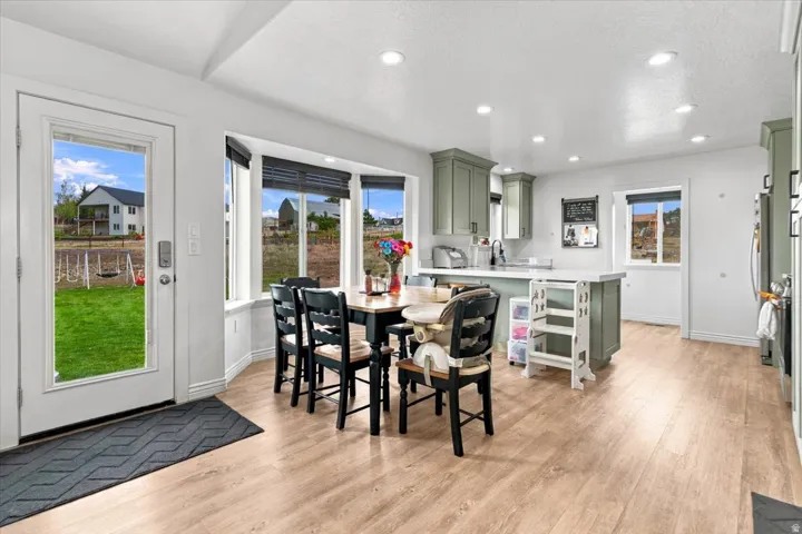 Wood-finish flooring throughout, bay window with dark window treatments, recessed lighting, and pale green cabinetry