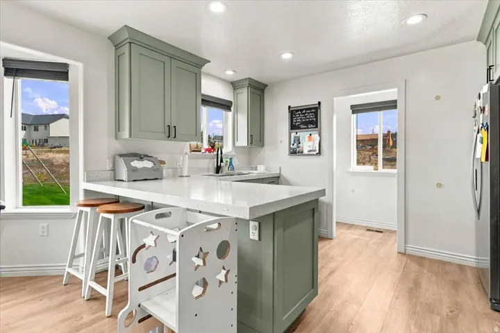 Kitchen featuring light wood-finish flooring, recessed lighting, white countertops, and sage green cabinetry with black hardware