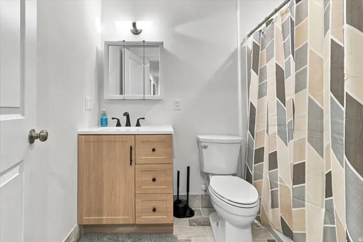 Wood-finish vanity with a white countertop and matte black fixtures, medicine cabinet with integrated lighting, and tile flooring