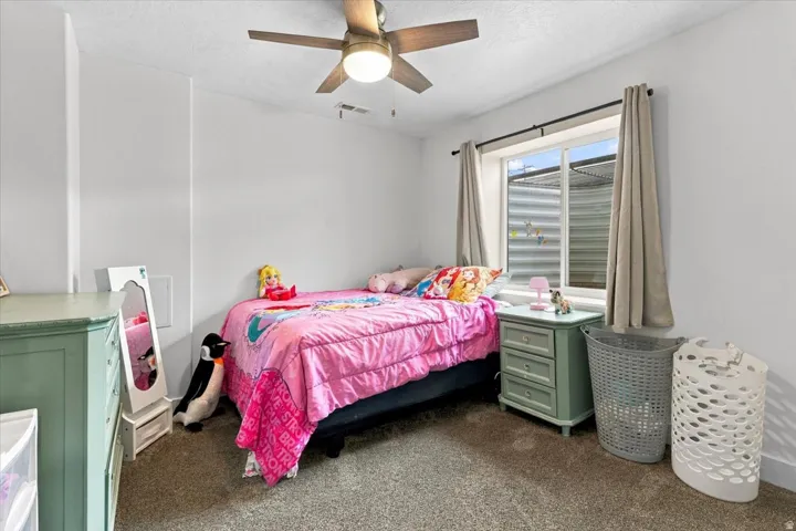 Bedroom featuring a ceiling fan with integrated lighting, carpeted flooring, and a window with white trim