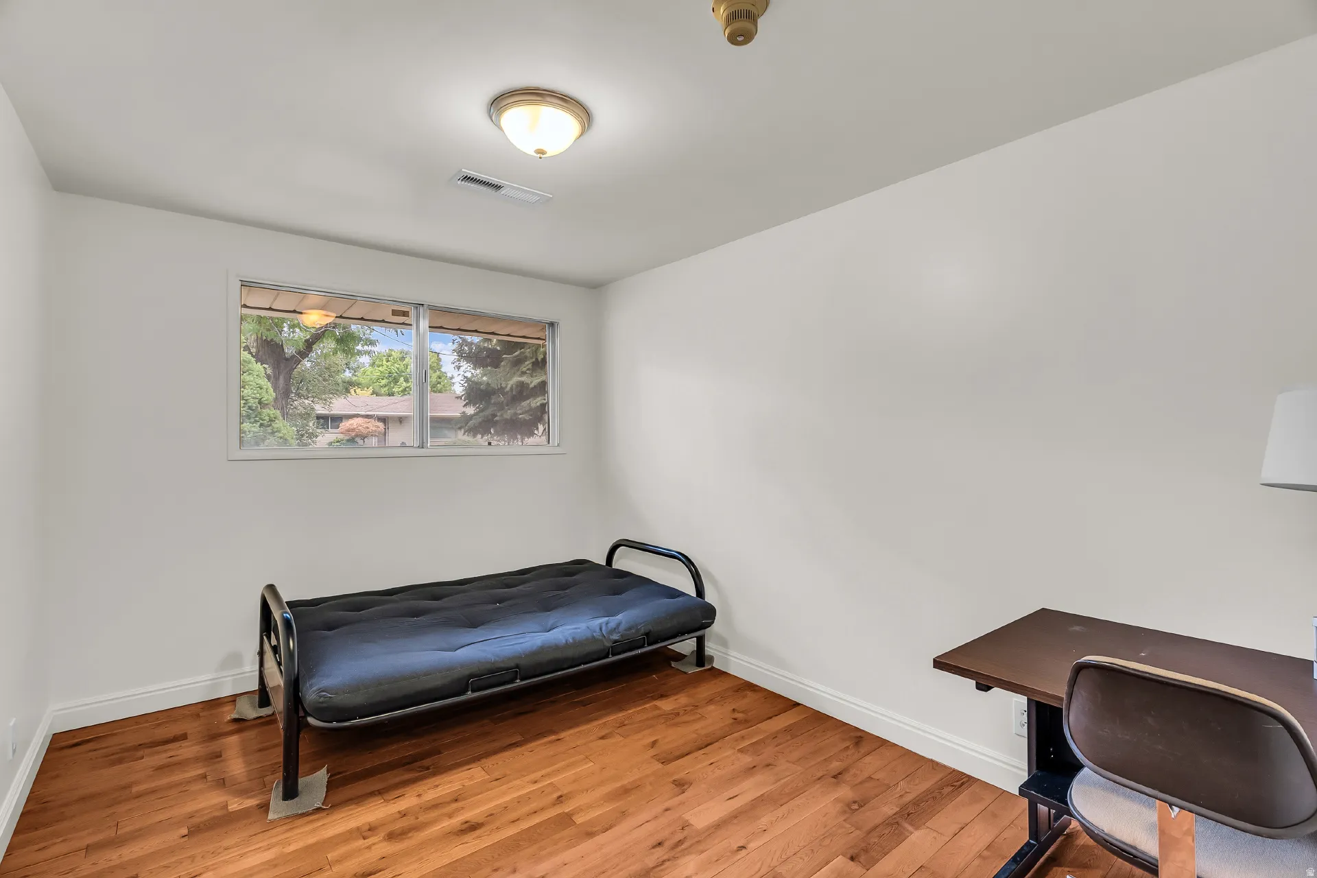 Wood-finish flooring with white baseboards, a window with exterior views, and an overhead flush-mount light fixture