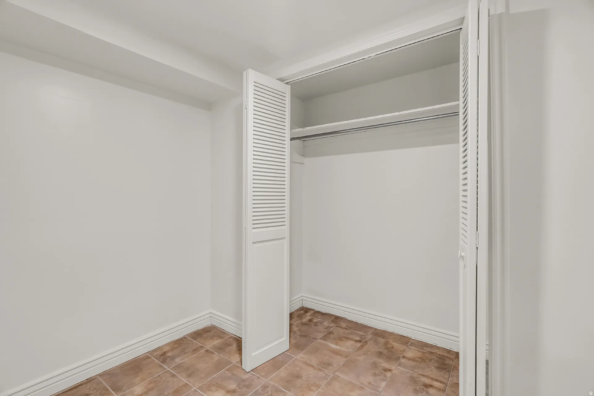 Louvered bi-fold closet doors, integrated hanging rod, and neutral ceramic tile flooring
