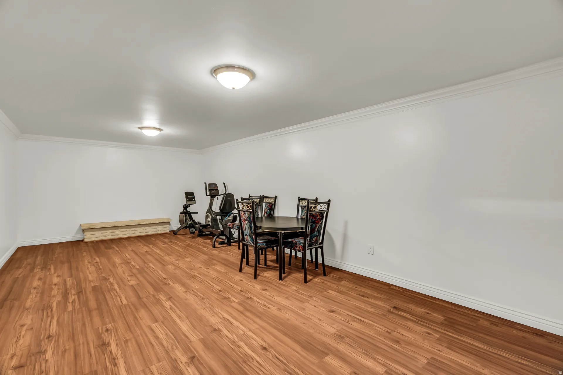 Spacious room featuring wood-finish flooring, white walls, and crown molding