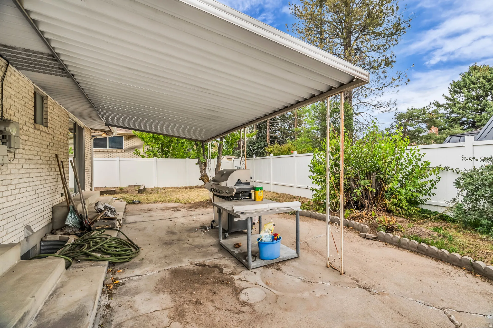 Covered patio with concrete flooring, white brick exterior, and a white privacy fence