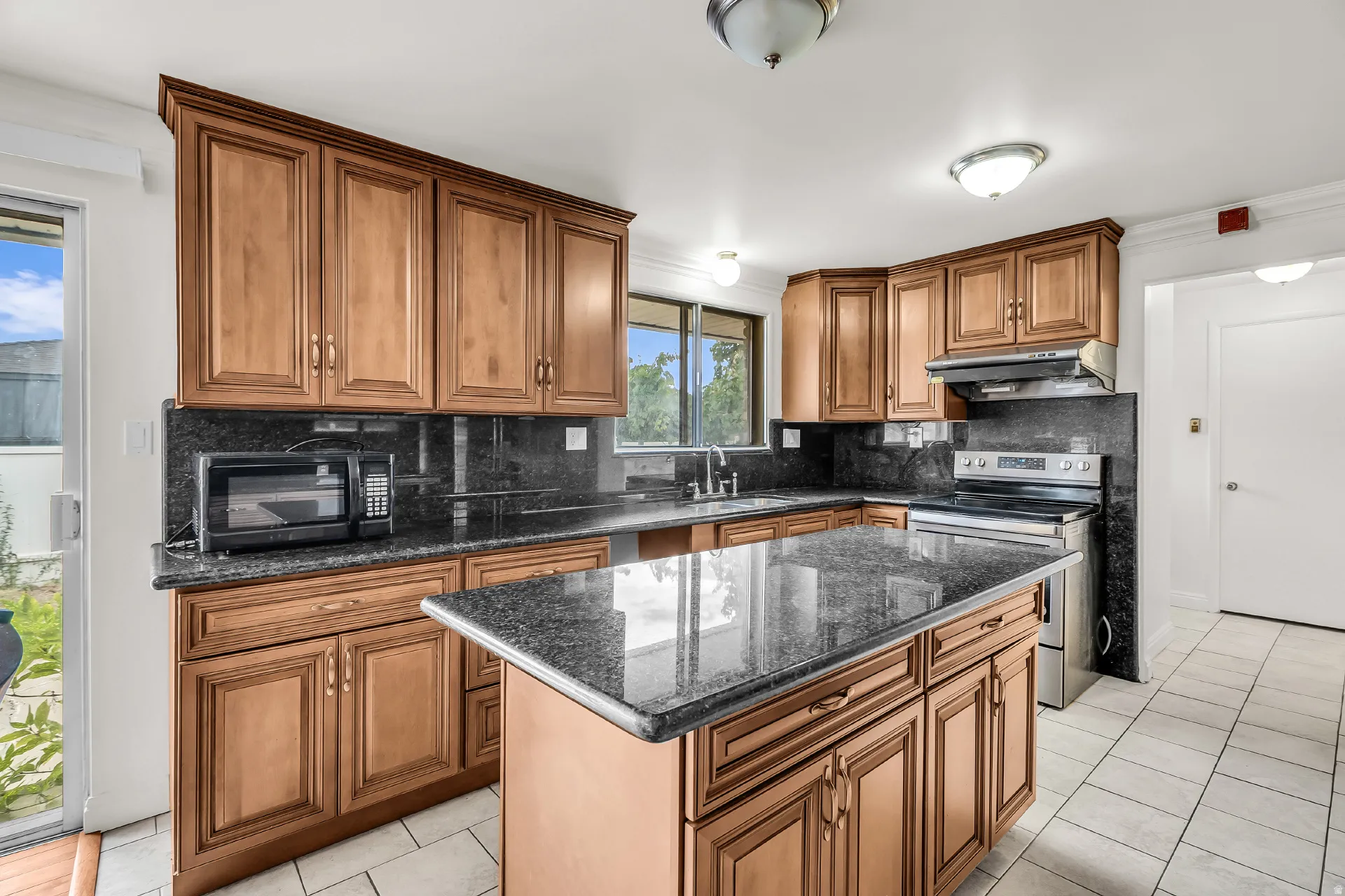 Kitchen featuring wood cabinetry, dark stone countertops, tile flooring, stainless steel range, and a central island