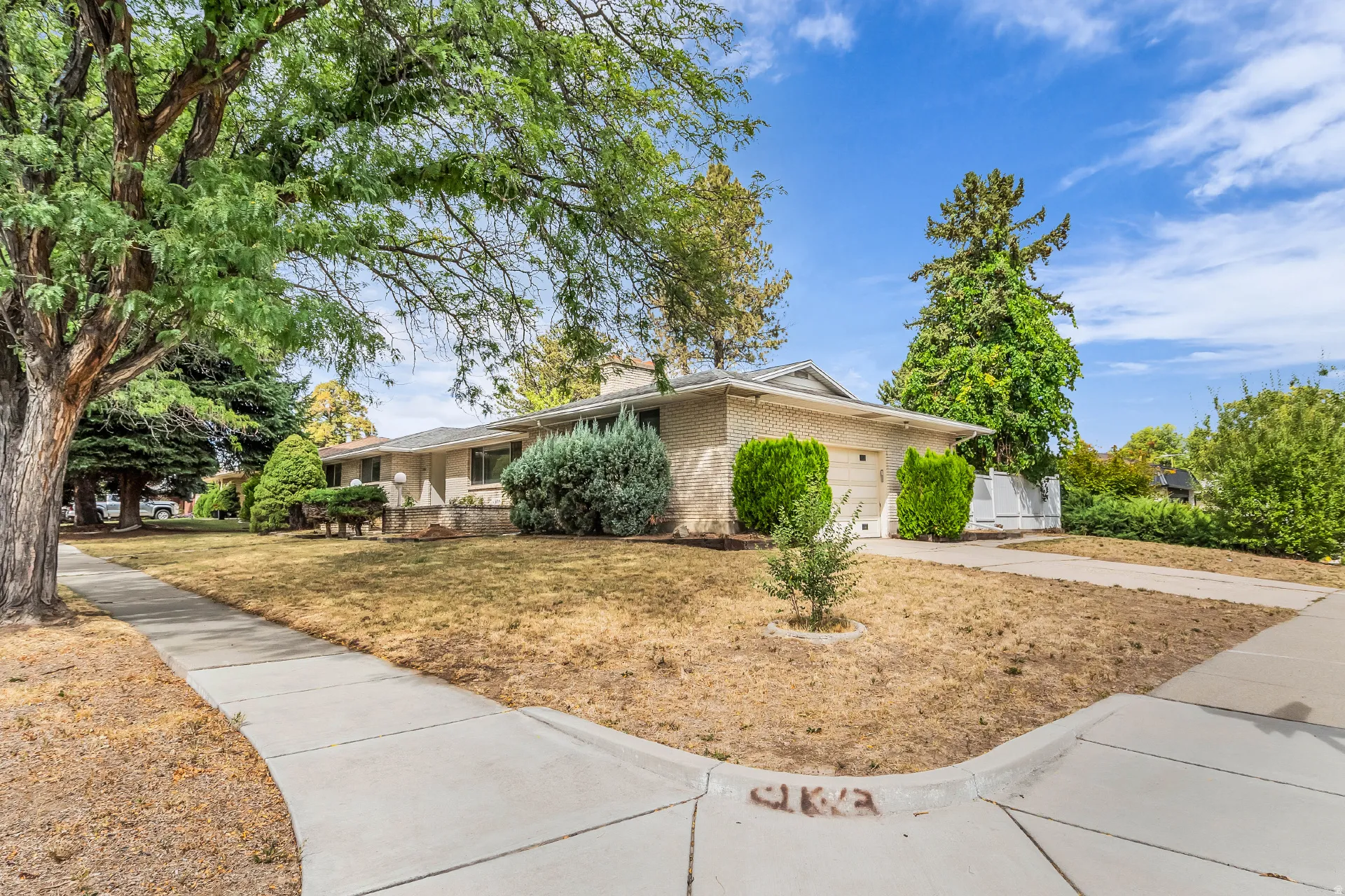 Ranch-style exterior with a light brick facade, attached garage, and mature trees framing the property