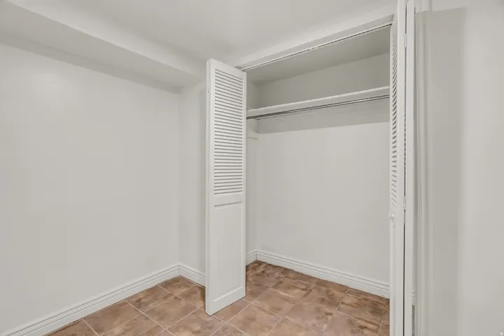 Louvered bi-fold closet doors, integrated hanging rod, and neutral ceramic tile flooring