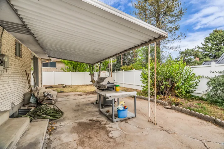 Covered patio with concrete flooring, white brick exterior, and a white privacy fence