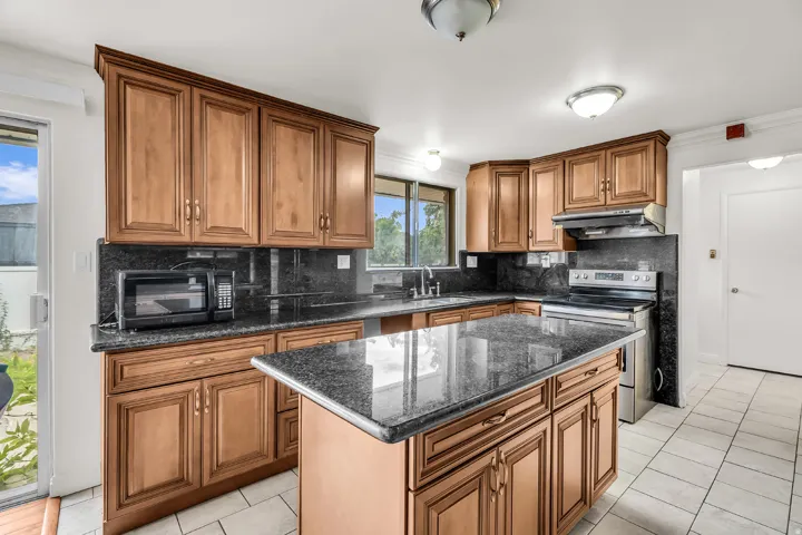 Kitchen featuring wood cabinetry, dark stone countertops, tile flooring, stainless steel range, and a central island