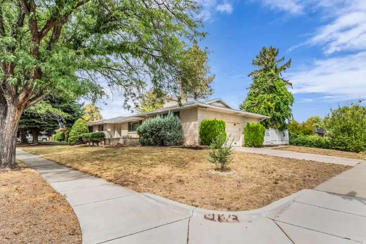 Ranch-style exterior with a light brick facade, attached garage, and mature trees framing the property