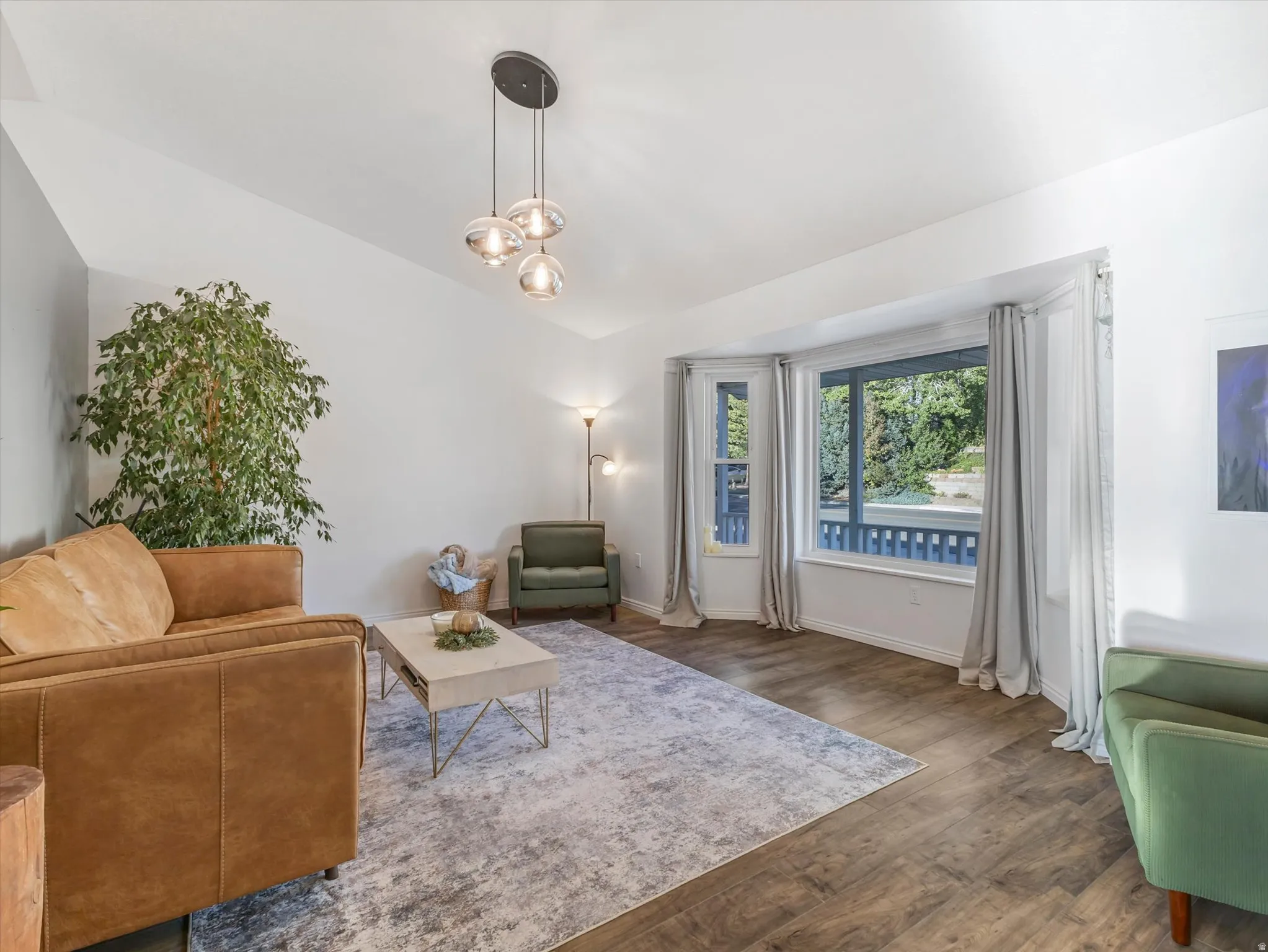 Vaulted ceiling, wood-finish flooring, bay window, and a contemporary three-light pendant fixture
