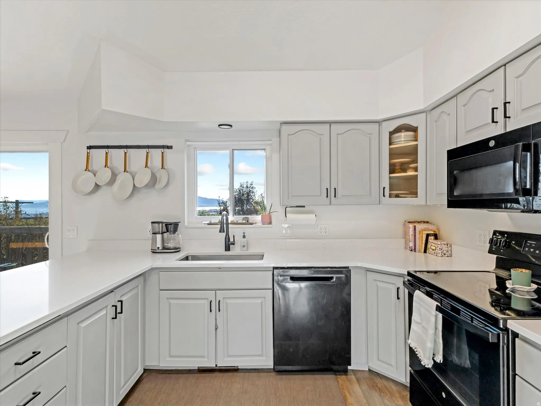 Kitchen featuring light-toned cabinetry, white countertops, stainless steel sink, black appliances, and wood-finish flooring