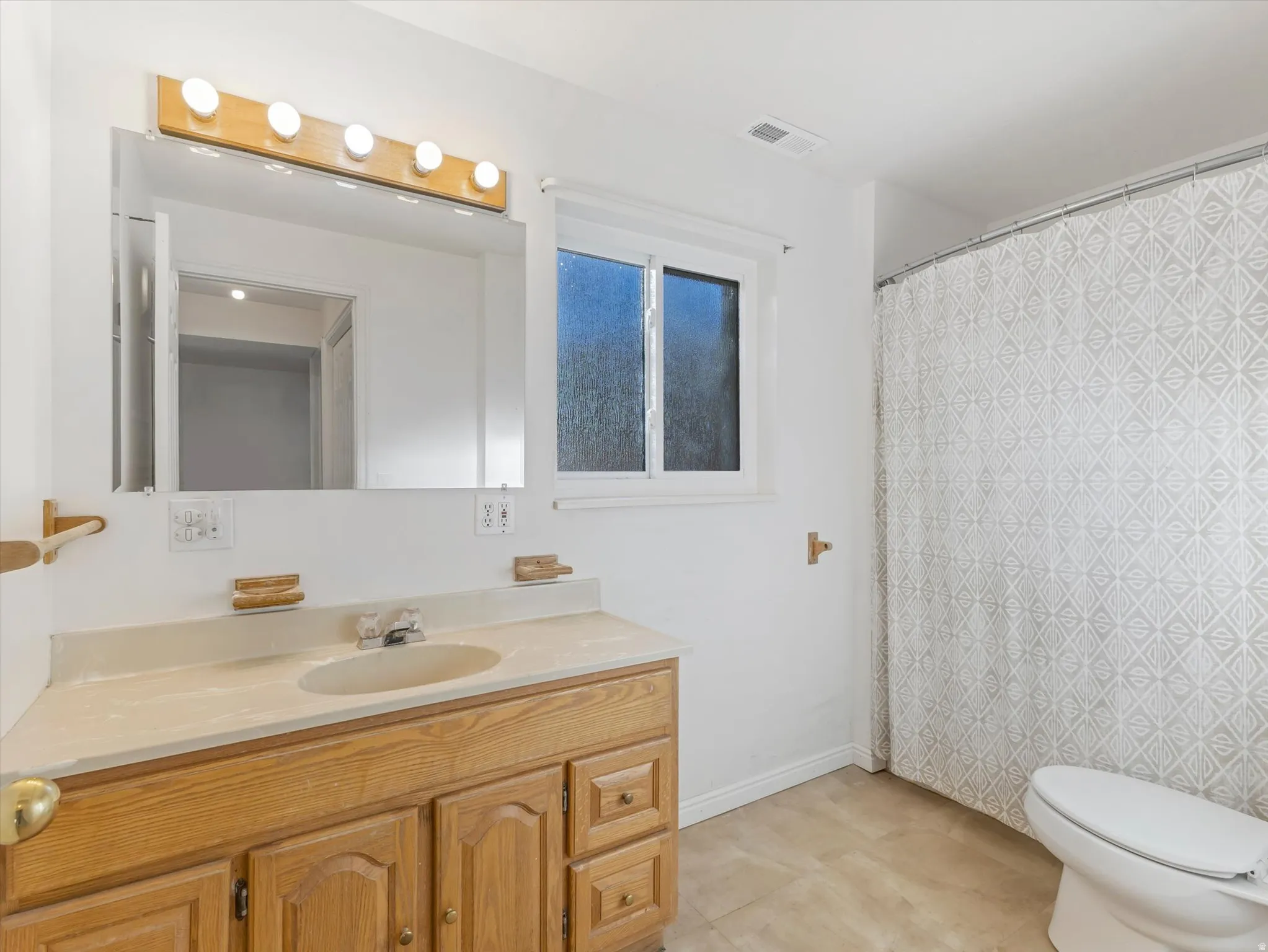 Wood-finish vanity with a built-in sink, wall-mounted mirror, and overhead vanity lighting