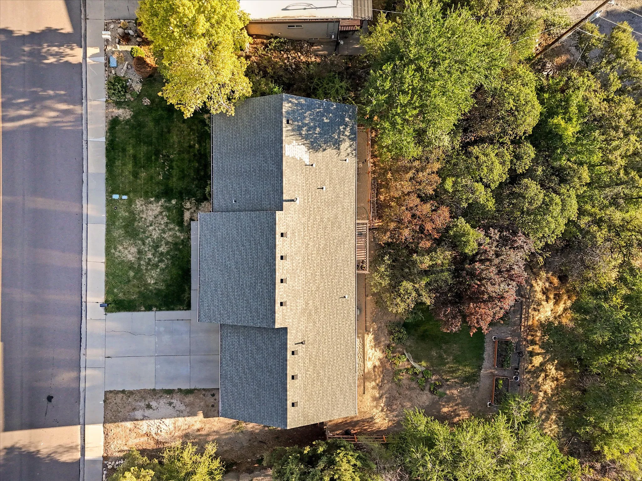 Pitched shingle roof, paved driveway, landscaped front yard, adjacent wooded area, rear garden beds
