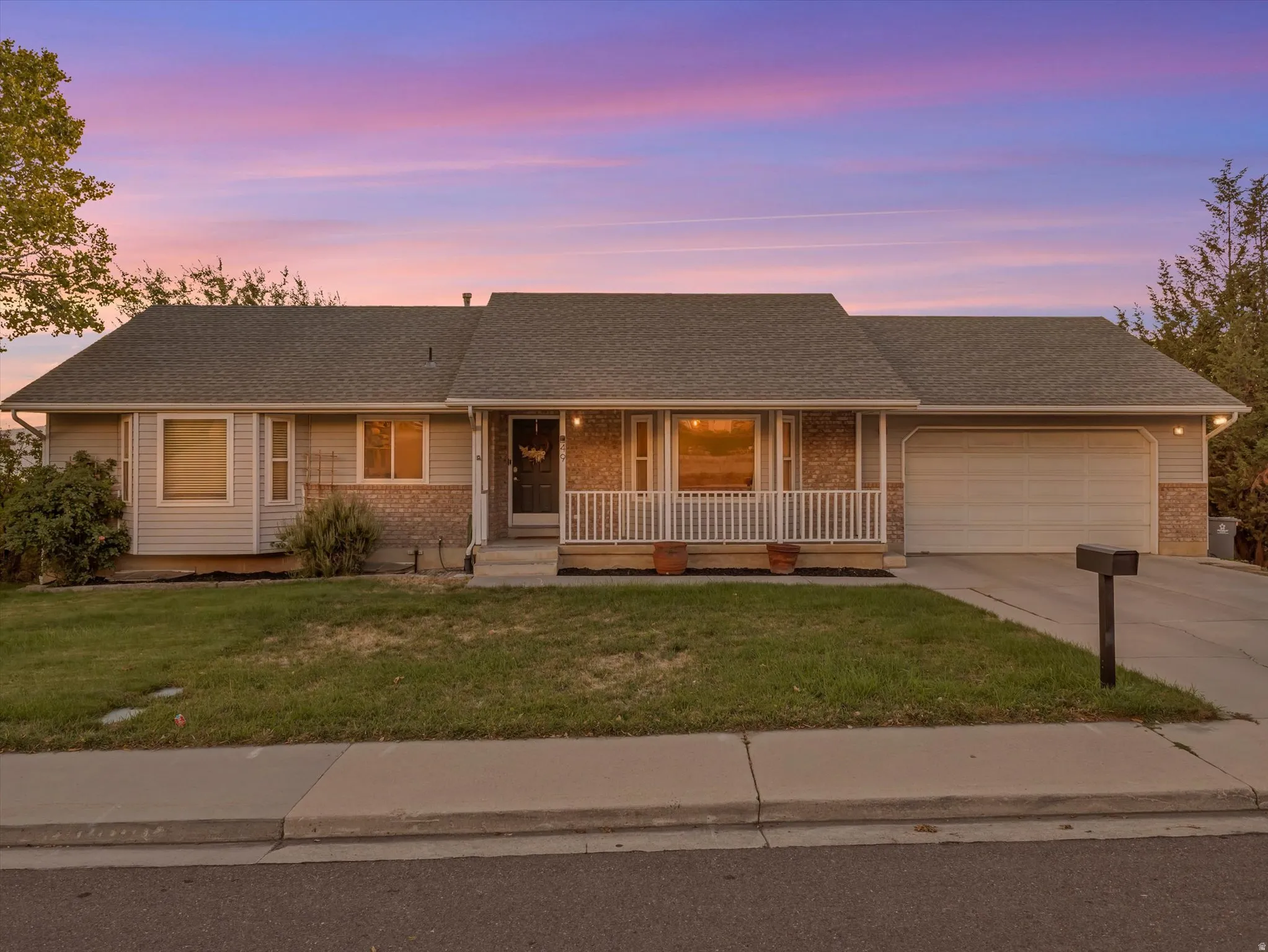 Ranch-style residence featuring a covered front porch with white railings, a two-car garage, and a concrete driveway
