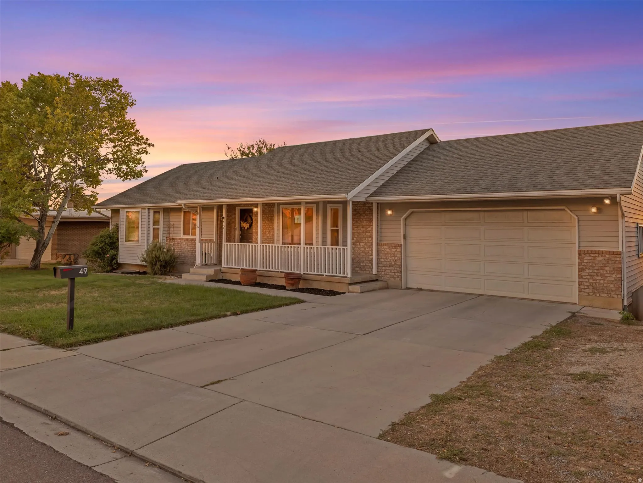Exterior featuring siding and brick accents, an attached garage, a covered front porch with white railings, and a concrete driveway