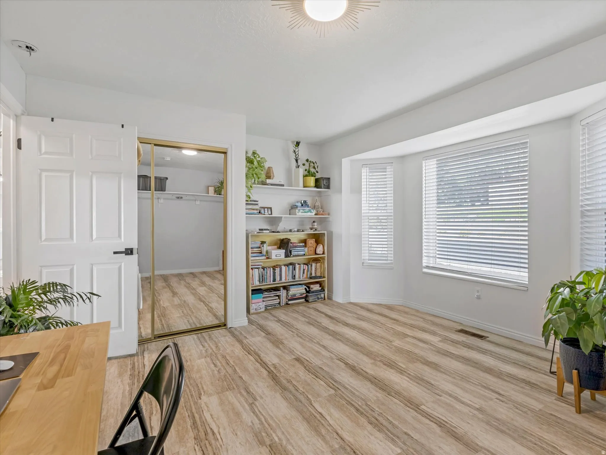 Wood-finish flooring, bay windows with blinds, wall-mounted shelving, and a closet with sliding mirrored doors