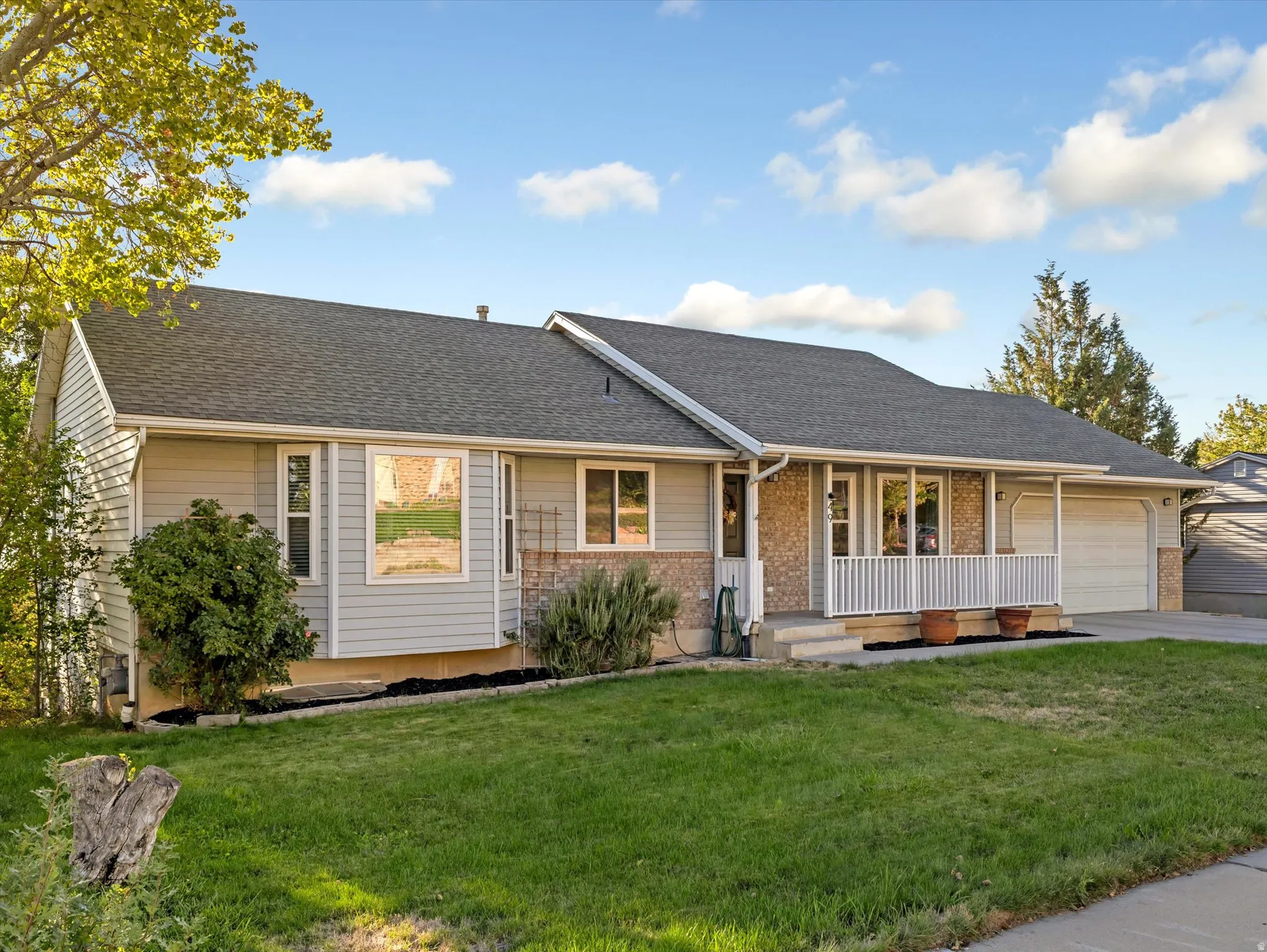 Single-story home featuring light gray siding, a covered front porch with white railing, a two-car garage, and a bay window