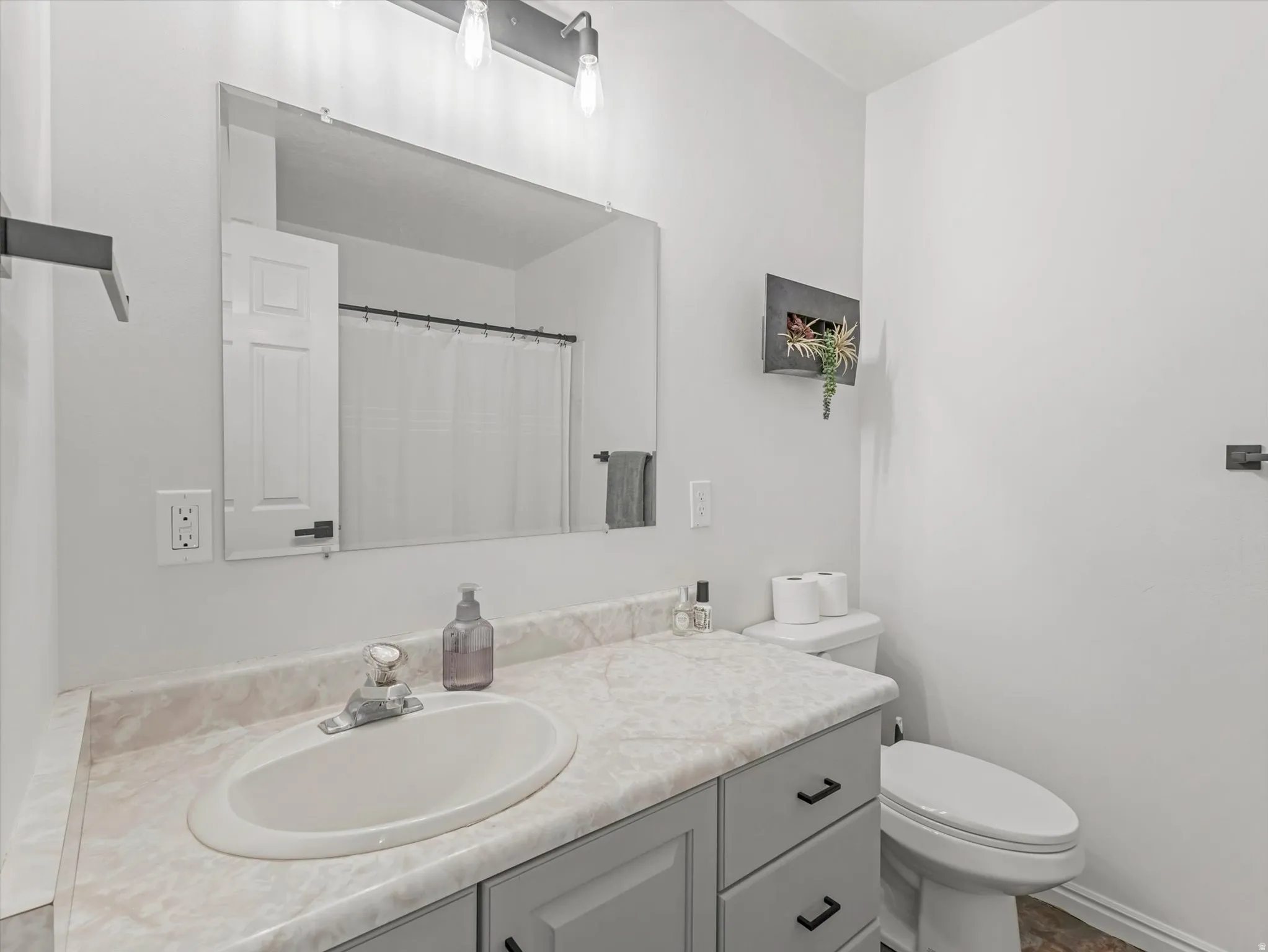 Bathroom vanity featuring a single basin sink, laminate countertop, and gray cabinetry with black hardware