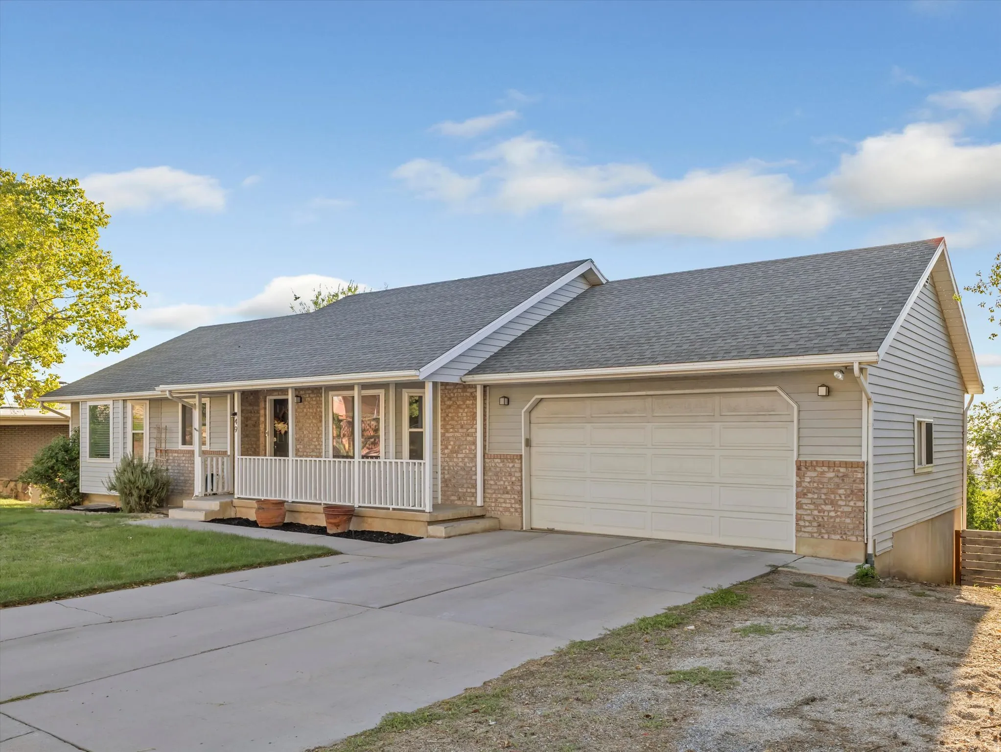 Exterior featuring light gray siding, brick veneer accents, a shingled roof, an attached two-car garage, and a covered front porch with white railings