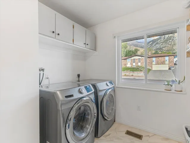 White upper cabinetry with dark hardware, white walls, white-framed window, and light-toned flooring