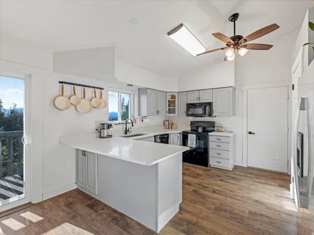 Kitchen with wood-finish flooring, white countertops, gray cabinetry, and a black appliance suite