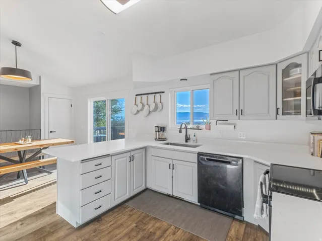 Kitchen featuring wood-finish flooring, white countertops, gray cabinetry, a stainless steel sink with a matte black faucet, and a sliding glass door