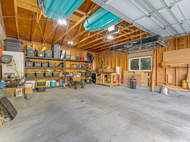 Expansive garage featuring a concrete floor, exposed wood beam ceiling, built-in shelving, and a prominent window