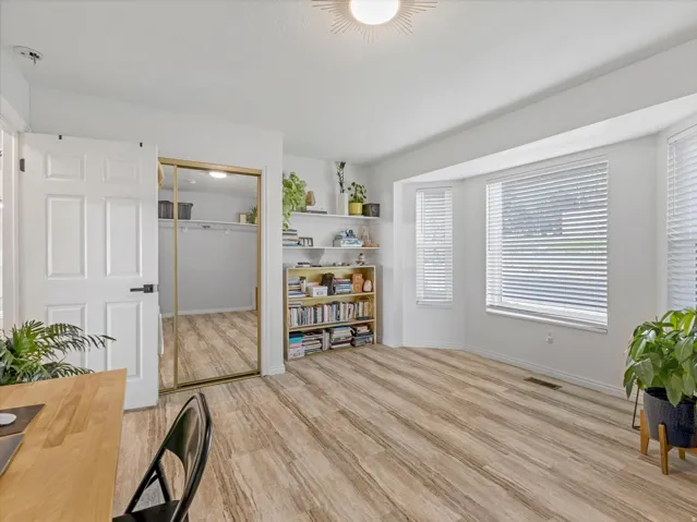 Wood-finish flooring, bay windows with blinds, wall-mounted shelving, and a closet with sliding mirrored doors
