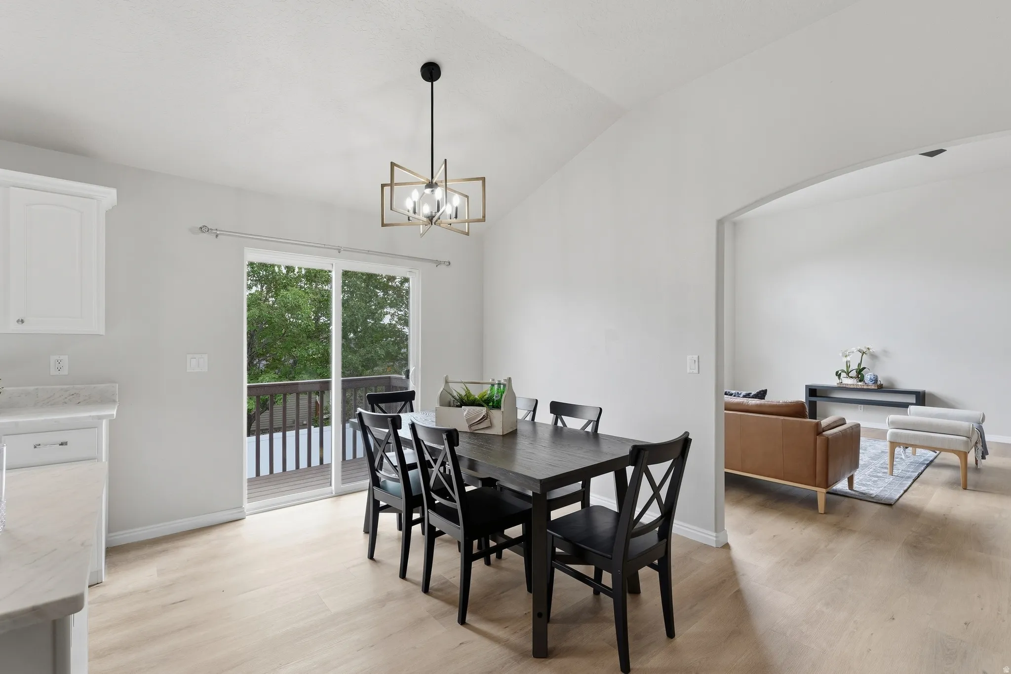 Vaulted ceilings with a geometric chandelier, wood-finish LVP flooring, sliding glass doors to outdoor deck, and an arched entryway