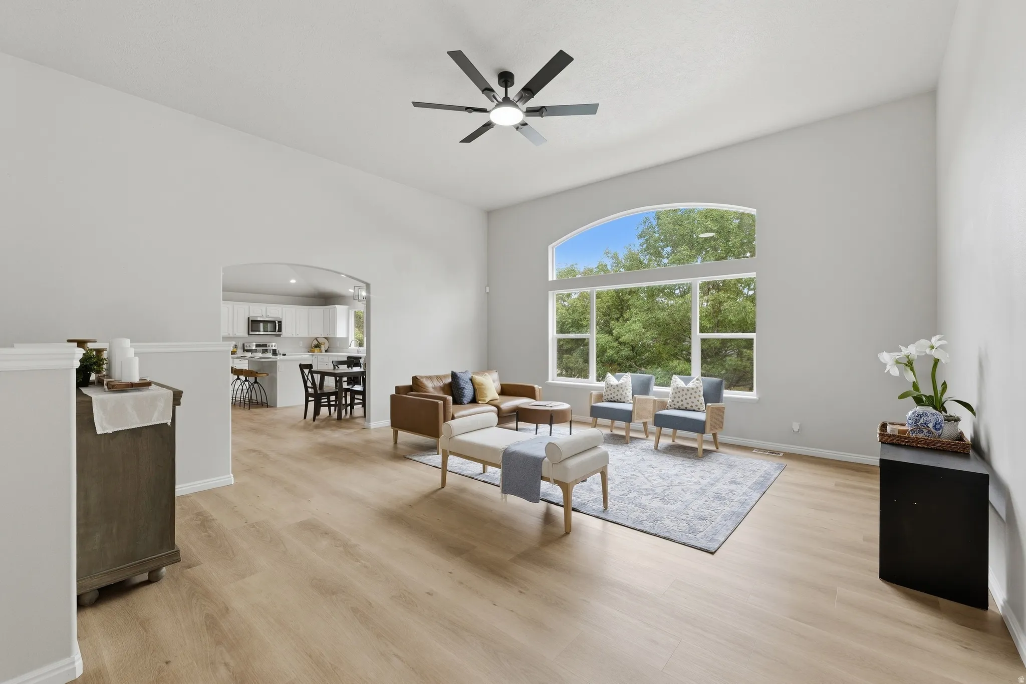 Vaulted ceilings with a ceiling fan, arched entryway, a large picture window, and wood-finish LVP flooring