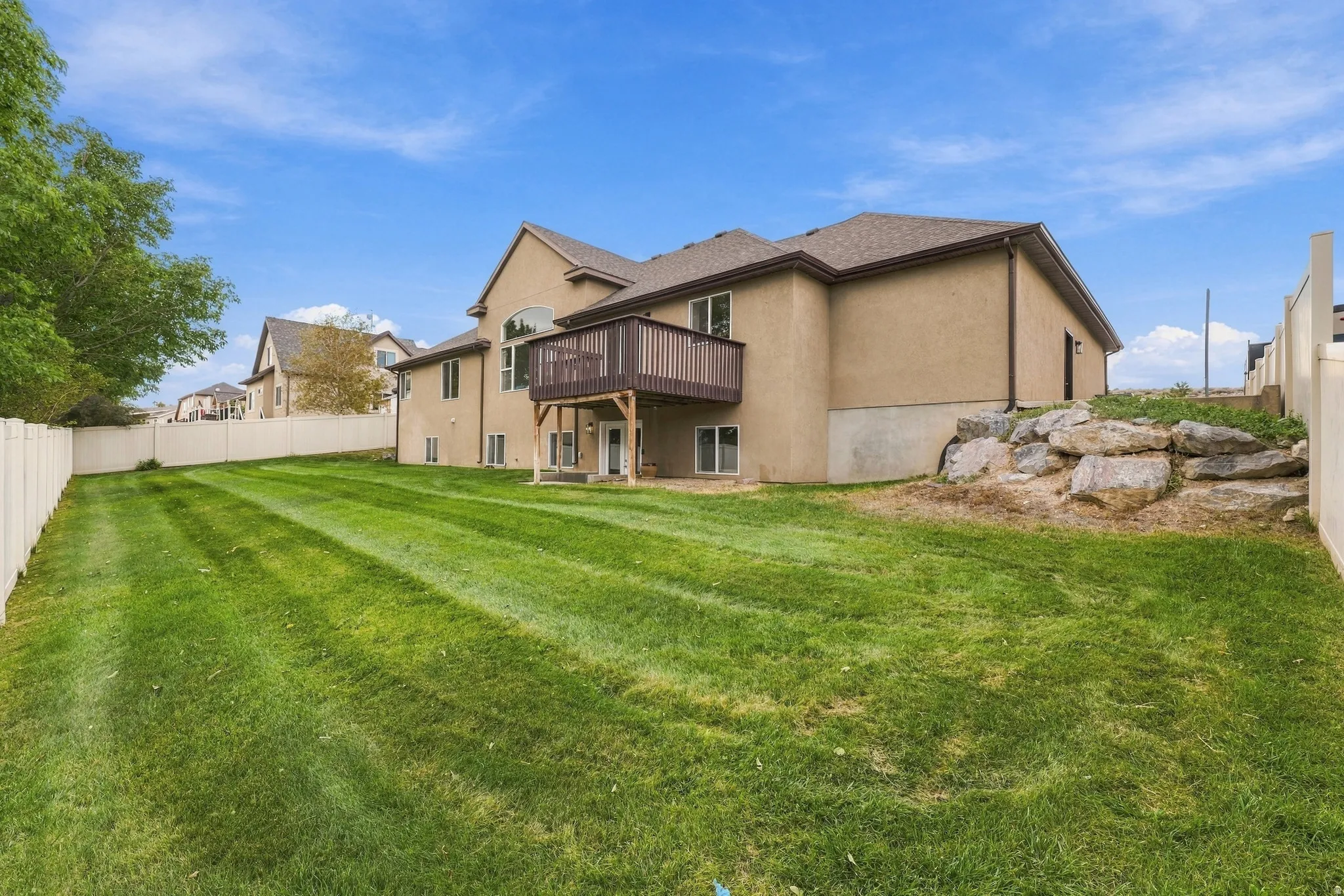 Expansive backyard with a manicured lawn, a second-story wood deck, basement entry, and a stucco exterior