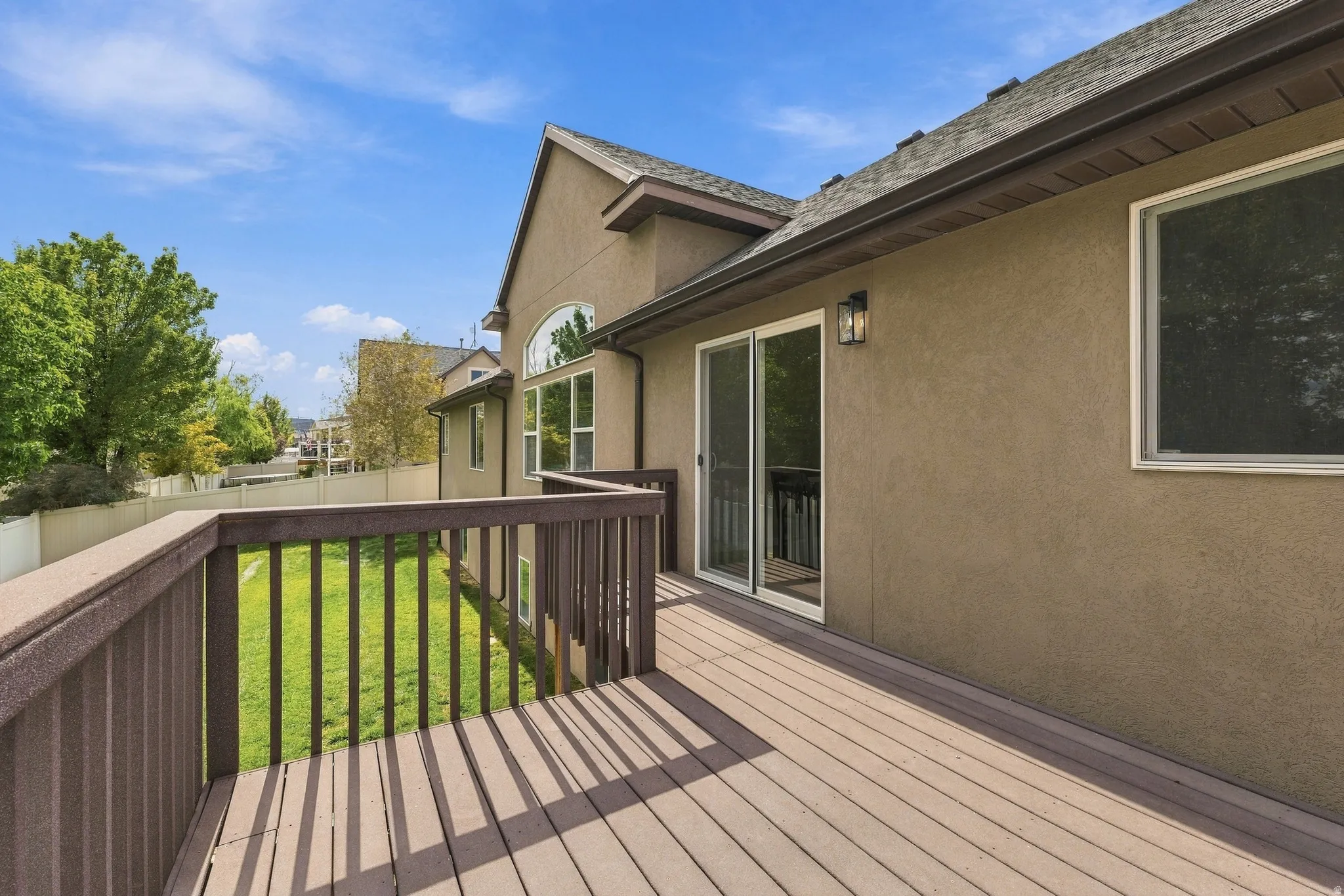 Expansive backyard deck with composite decking and dark railings, stucco siding, sliding glass door access
