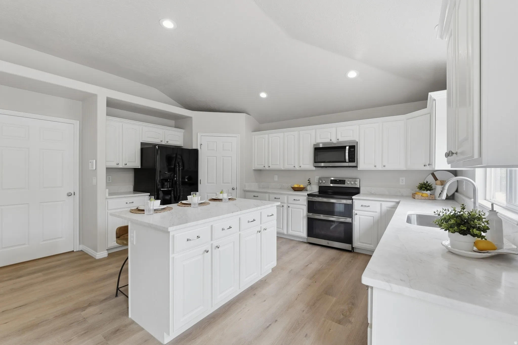 Kitchen featuring a central island, white cabinetry, integrated stainless steel appliances, light-toned quartz countertops, and wood-finish LVP flooring