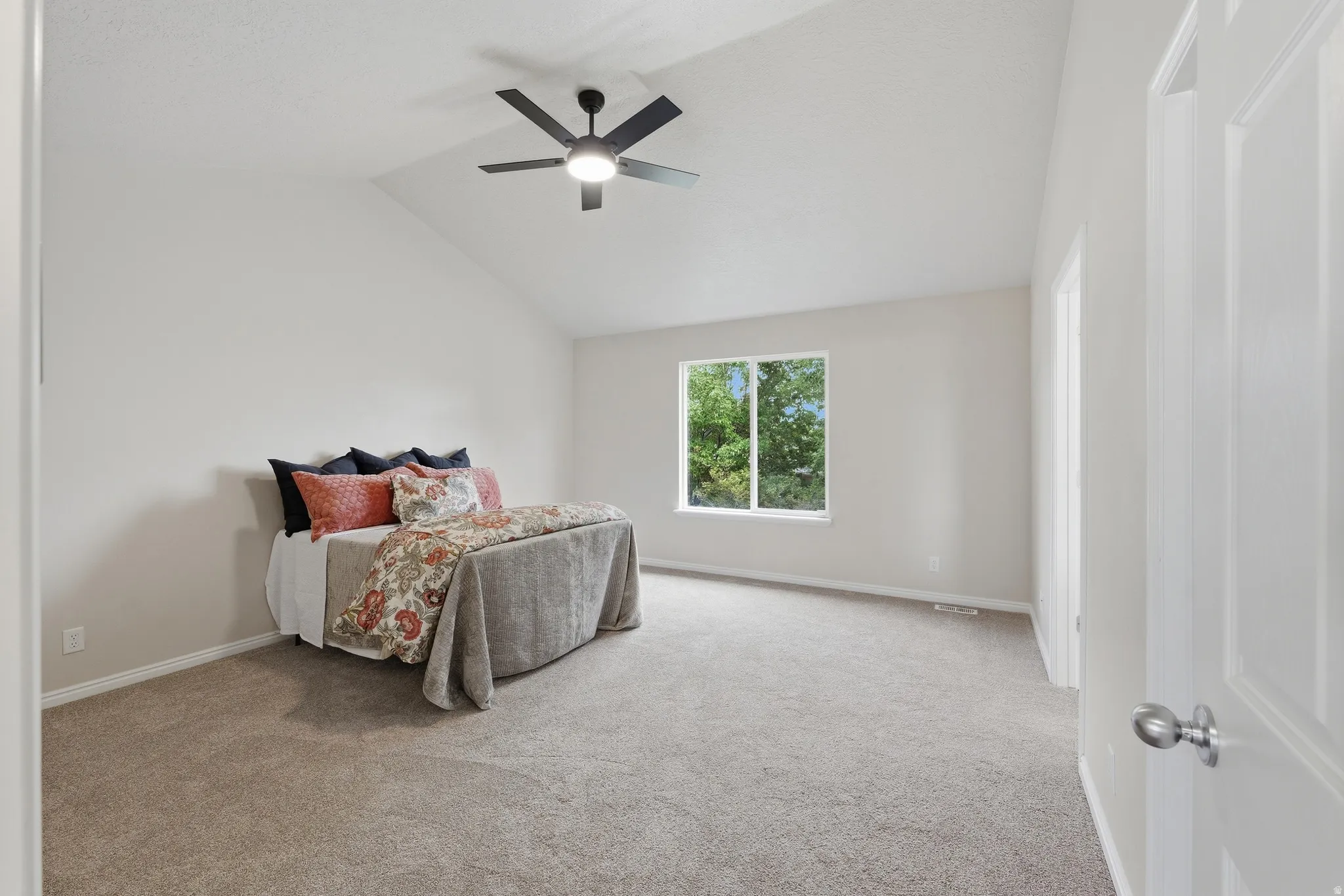 Primary bedroom with vaulted ceiling and ceiling fan, plush carpeting, and a large window