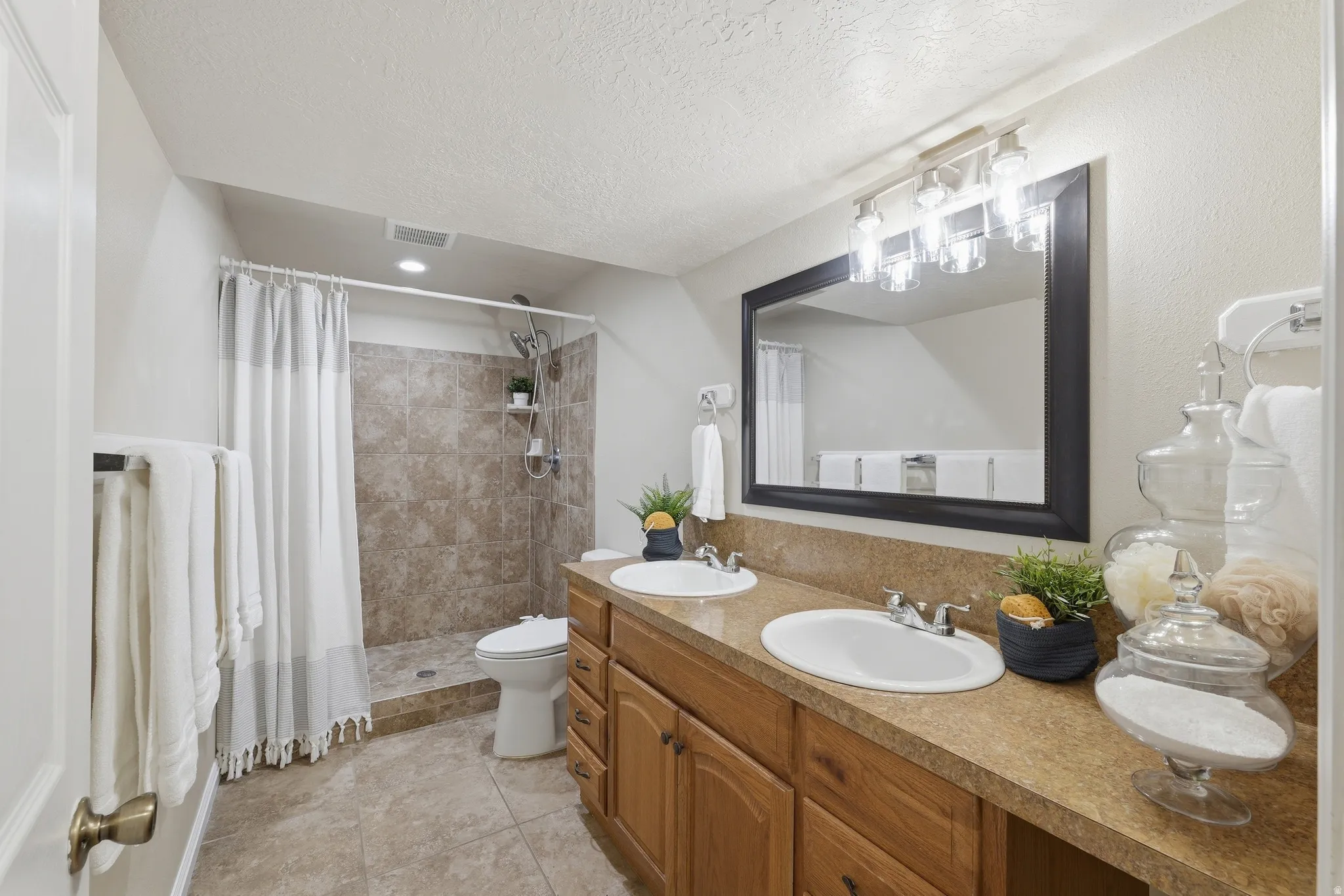 3/4 bath with dual vanity, wood-finish cabinetry, a large framed mirror, and a tiled walk-in shower