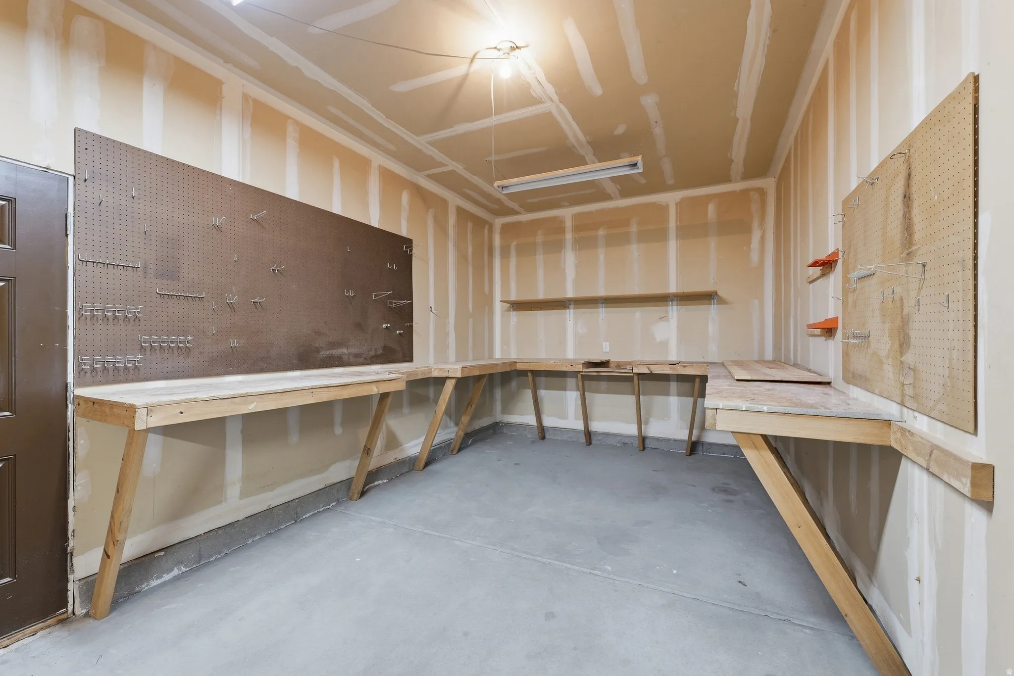 Extra depth in 3rd bay with Integrated workbench with pegboard organization, additional wall shelving, and concrete flooring