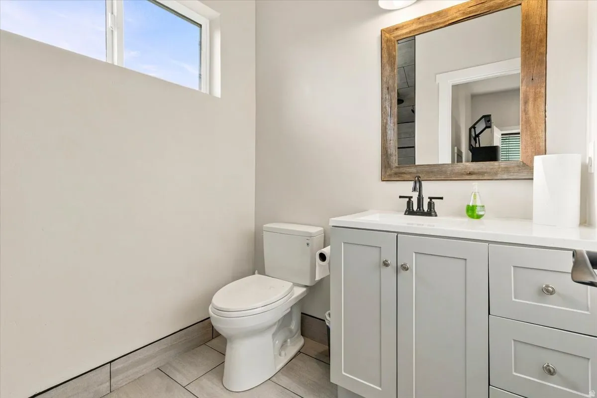 White vanity with light gray shaker-style cabinetry, a white countertop, and a dark-finish faucet