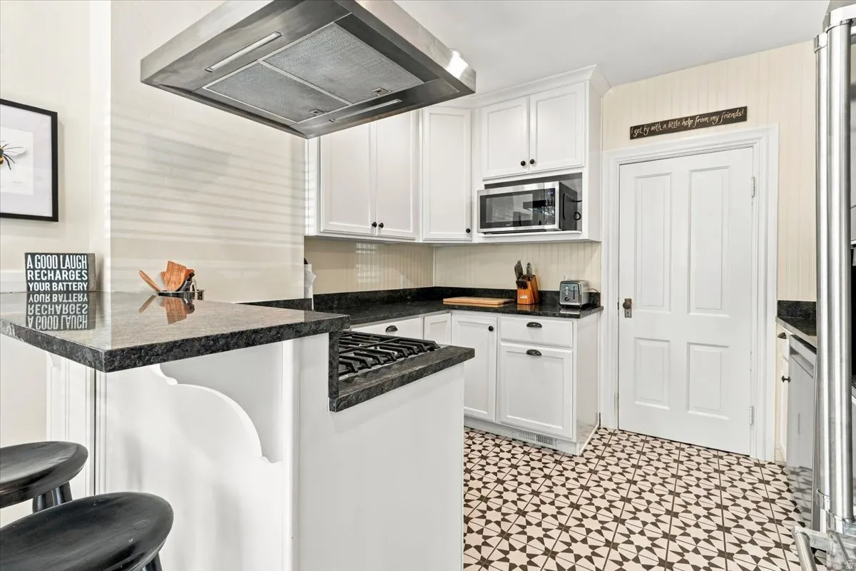 White cabinetry with dark hardware, built-in microwave, stainless steel range hood, patterned floor tile, and a four-panel interior door