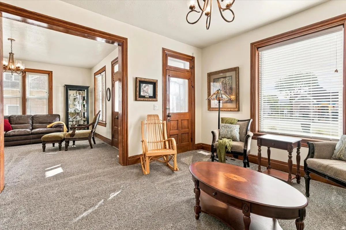 Carpeted living space featuring substantial wood trim, white walls, and a prominent window with horizontal blinds