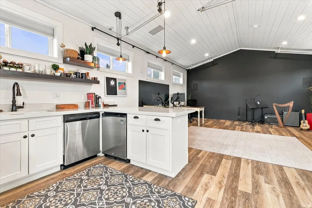 White shaker cabinetry, stainless steel appliances, wood-finish flooring, white countertops, and vaulted ceilings